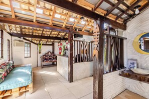 A rustic interior with a wooden ceiling, a bench with floral upholstery, and a white brick wall. - Pousada Lua Chalés Maresias (São Sebastião)