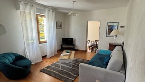 Un salon comprenant un canapé, un fauteuil, un téléviseur et un coin repas.