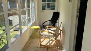 Une pièce baignée de lumière, avec un sol carrelé, une chaise en bois, une table jaune et une porte dont les panneaux sont ornés de motifs en verre.