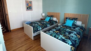 Une chambre avec deux lits simples, des têtes de lit en bois, un luminaire suspendu et un plancher en bois.