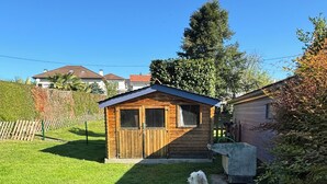 Une petite cabane en bois avec un toit en pente, une cour clôturée et un chien assis sur l’herbe.