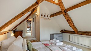 Un dormitorio con techo inclinado, vigas de madera, una cama con ropa blanca, un aparador y un radiador.