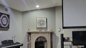 A room with a fireplace, a piano, a television, and a projector screen. - Elegant Retreat With Heated Pool Baseball Retreat  (Marietta)