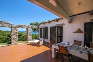 Une terrasse avec une table dressée pour le dîner, des piliers en pierre et une vue sur la mer.