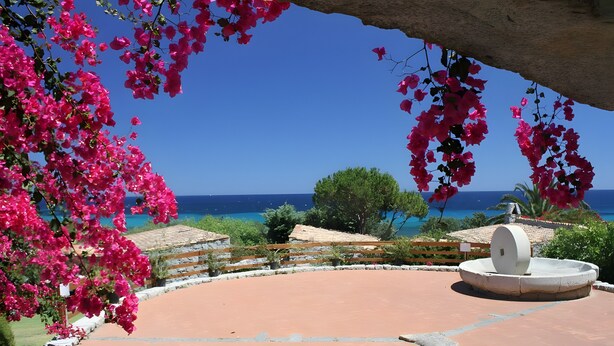 Un patio con una fuente, vistas al mar y flores de buganvilla rosadas.
