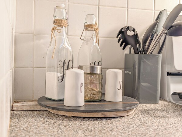 Una encimera de cocina con dos botellas de vidrio, un recipiente metálico y un organizador de utensilios.