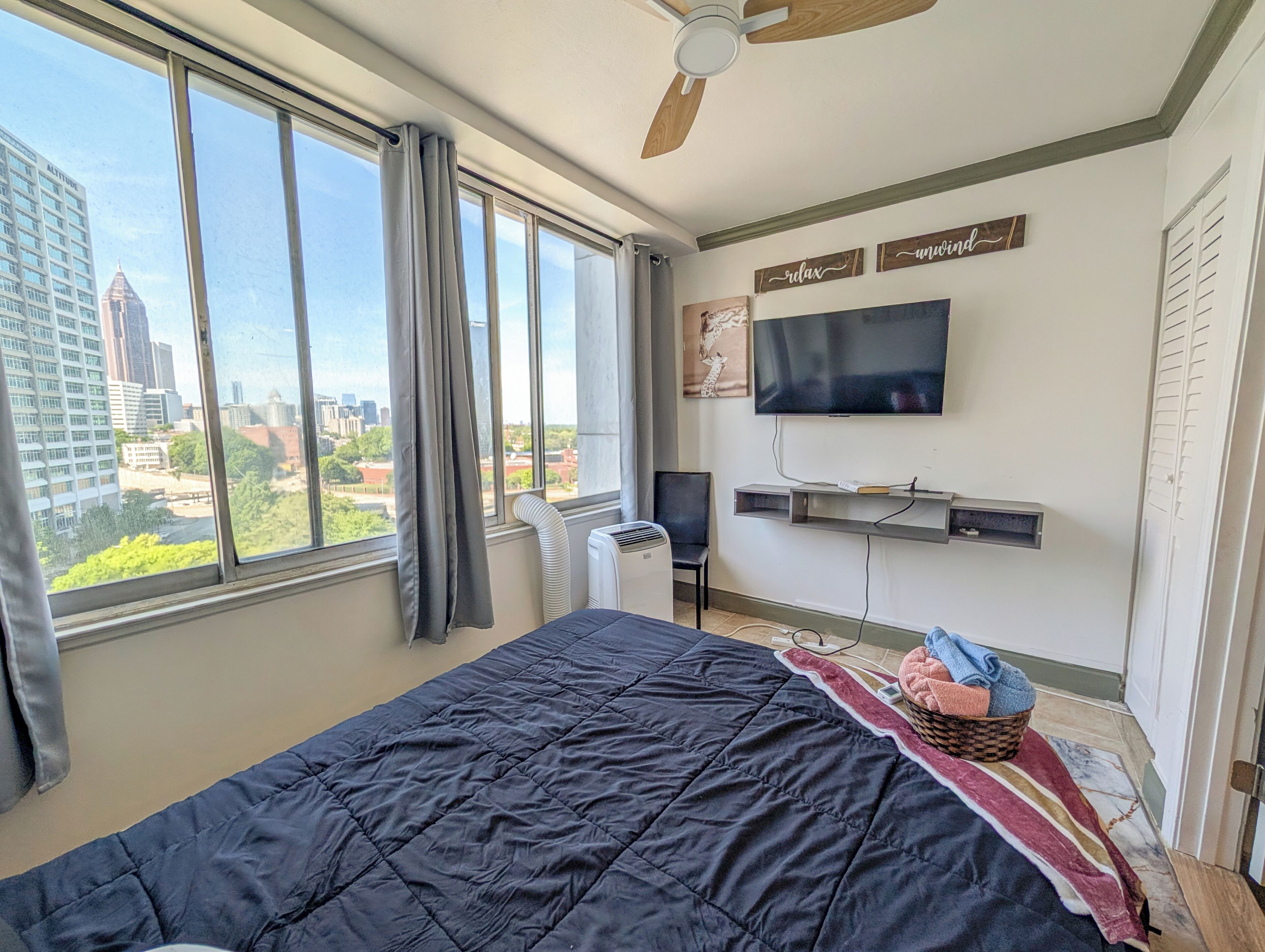 A bedroom with a large window, a bed, a TV, a chair, and a heater.