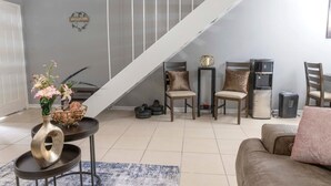 A living room with a staircase, a sofa, two chairs, a coffee table, and a decorative vase with flowers.