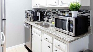 A modern kitchen with white cabinets, a granite countertop, a stainless steel sink, a microwave, and a coffee maker.
