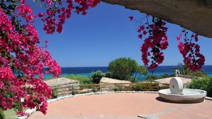 A courtyard with a fountain, surrounded by pink bougainvillea flowers, a clear blue sky, and a view of the sea. - Villa 'Casa 2' with Private Terrace, Garden, and Air Conditioning (Castiadas)