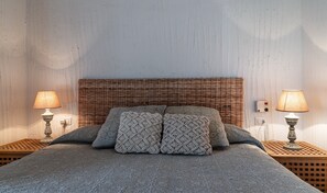 En säng med ett flätat sänggavel, två sänglampor och mönstrade kuddar.