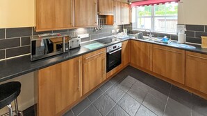 Une cuisine moderne avec des meubles en bois, un plan de travail noir, un four encastré et une fenêtre agrémentée d’une lambrequin rouge.