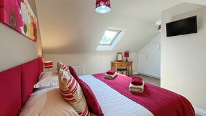 Une chambre à coucher avec un grand lit, un bureau, une chaise, un radiateur, une télévision et une lucarne.
