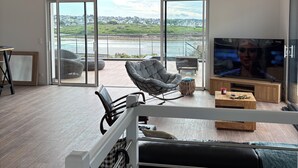 Un salon moderne doté d’un grand téléviseur, de sièges confortables et offrant une vue sur l’extérieur.