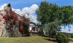 Edifici de pedra amb façana blanca, arc de pedra i un arbre al primer pla.