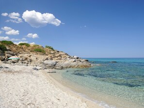 A beach with clear water, rocky terrain, and a colorful umbrella.