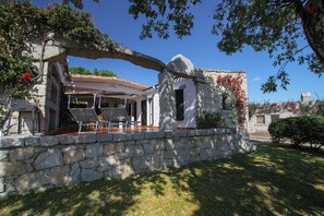 A stone-walled outdoor seating area with a pergola, a covered patio, and a stone structure with a window.