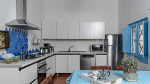 Une cuisine compacte avec des meubles blancs, une cuisinière en acier inoxydable, un four à micro-ondes et un lave-vaisselle. On y trouve également un coin repas avec une table dressée pour deux personnes et une nappe à motifs bleus.