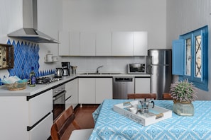 A compact kitchen with white cabinets, a stainless steel range, a microwave, and a dishwasher. There's a dining area with a table set for two and a blue patterned tablecloth.