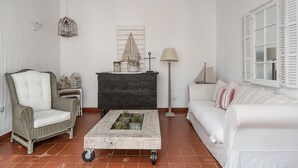 Un salon comprenant un fauteuil en osier, un canapé blanc, une table basse, un meuble et une lampe.