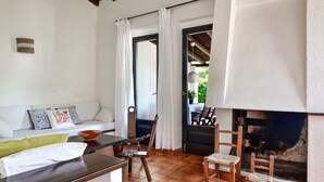 A living room with a sofa, chairs, a table, a fireplace, and a door leading outside. - Villa 'Salvi' with Private Terrace, Wi-Fi and Air Conditioning (Costa Rei)