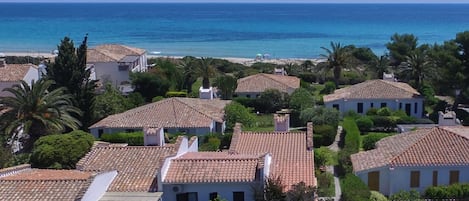 A coastal residential area with terracotta-tiled houses, a beach, and palm trees.