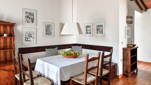 A dining area with a table set for four, surrounded by wooden chairs, a white tablecloth, and a bowl of fruit. - Villa 'Salvi' with Private Terrace, Wi-Fi and Air Conditioning (Costa Rei)
