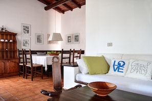 Una sala acogedora con una mesa de comedor de madera, sillas, un sofá con almohadones decorativos y una pared adornada con fotografías enmarcadas.