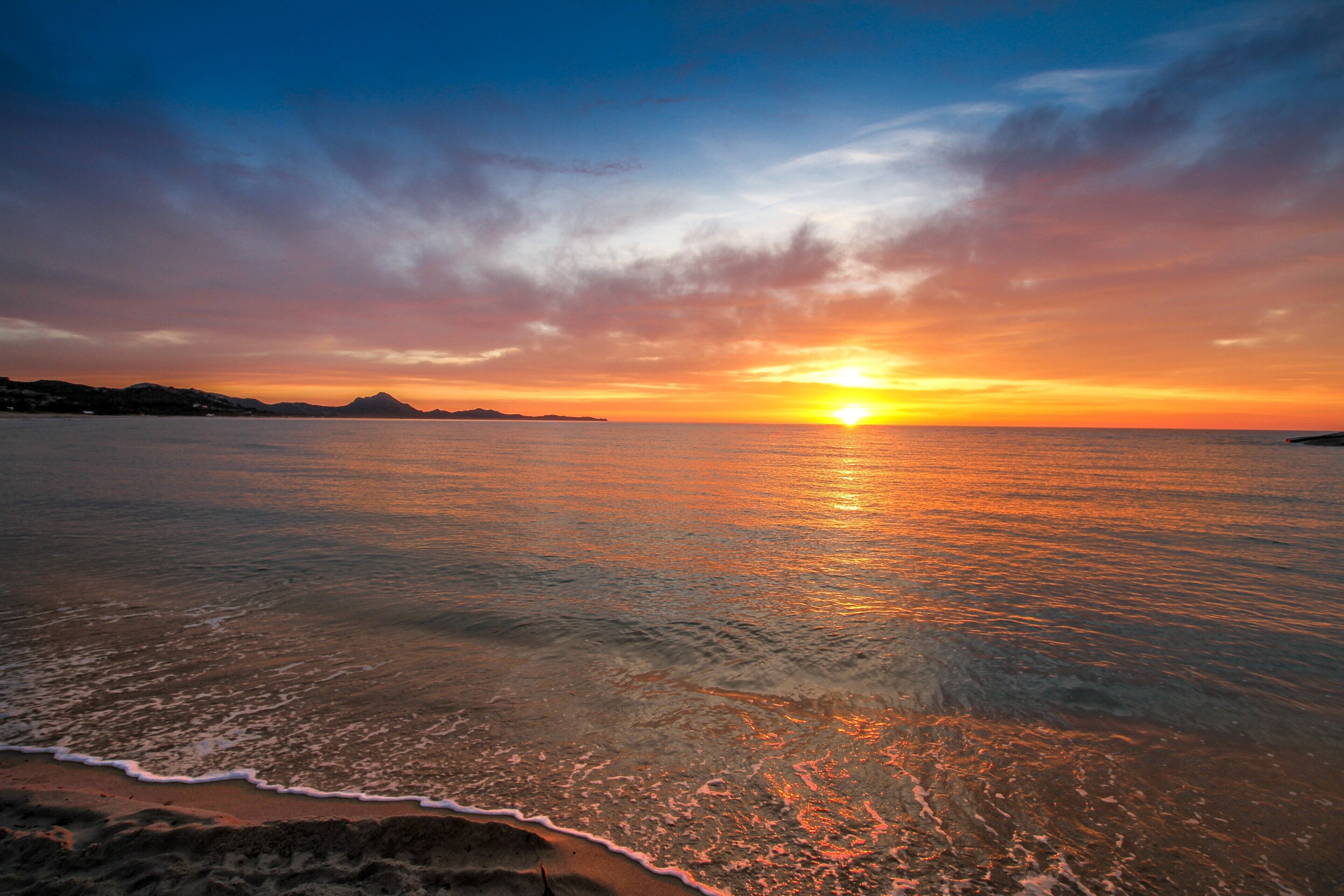 Ein Sonnenuntergang über einem ruhigen Meer mit einer fernen Küste.