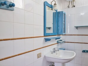 Une salle de bain avec des carreaux blancs, un lavabo blanc, un miroir avec un cadre bleu et un porte-serviettes.