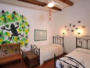 Une chambre avec deux lits, un banc en bois, une petite commode, une fresque murale et une carte encadrée.