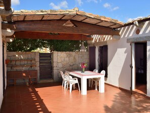 Une terrasse extérieure avec une table et des chaises, un mur en pierre et un banc en bois.