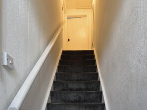 Eine enge Treppe mit Teppichstufen, die zu einer Tür führt.