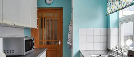 A kitchen with a microwave, sink, and wooden door.