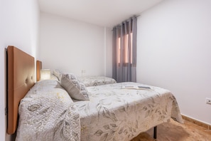 A bedroom with two beds, a headboard, a bedside table, and a window with curtains.