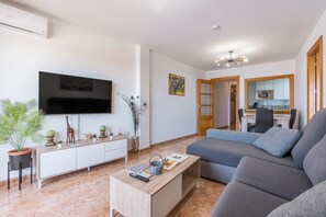 A modern living room with a flat-screen TV, a sofa, a coffee table, and a kitchen in the background.
