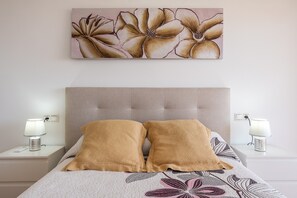 Une chambre à coucher comprenant un lit, deux tables de chevet, une lampe fixée au mur et une œuvre d’art à motifs floraux.