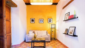 A living room with a sofa, a coffee table, and a floor lamp. There are three framed pictures on the wall and a shelf with books and a vase. - CASA MADERO (Tapalpa)