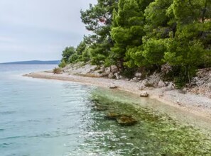 A coastal beach with clear shallow waters, rocky shoreline, and dense green trees. - Holiday Home House of the Sun (Sutivan)