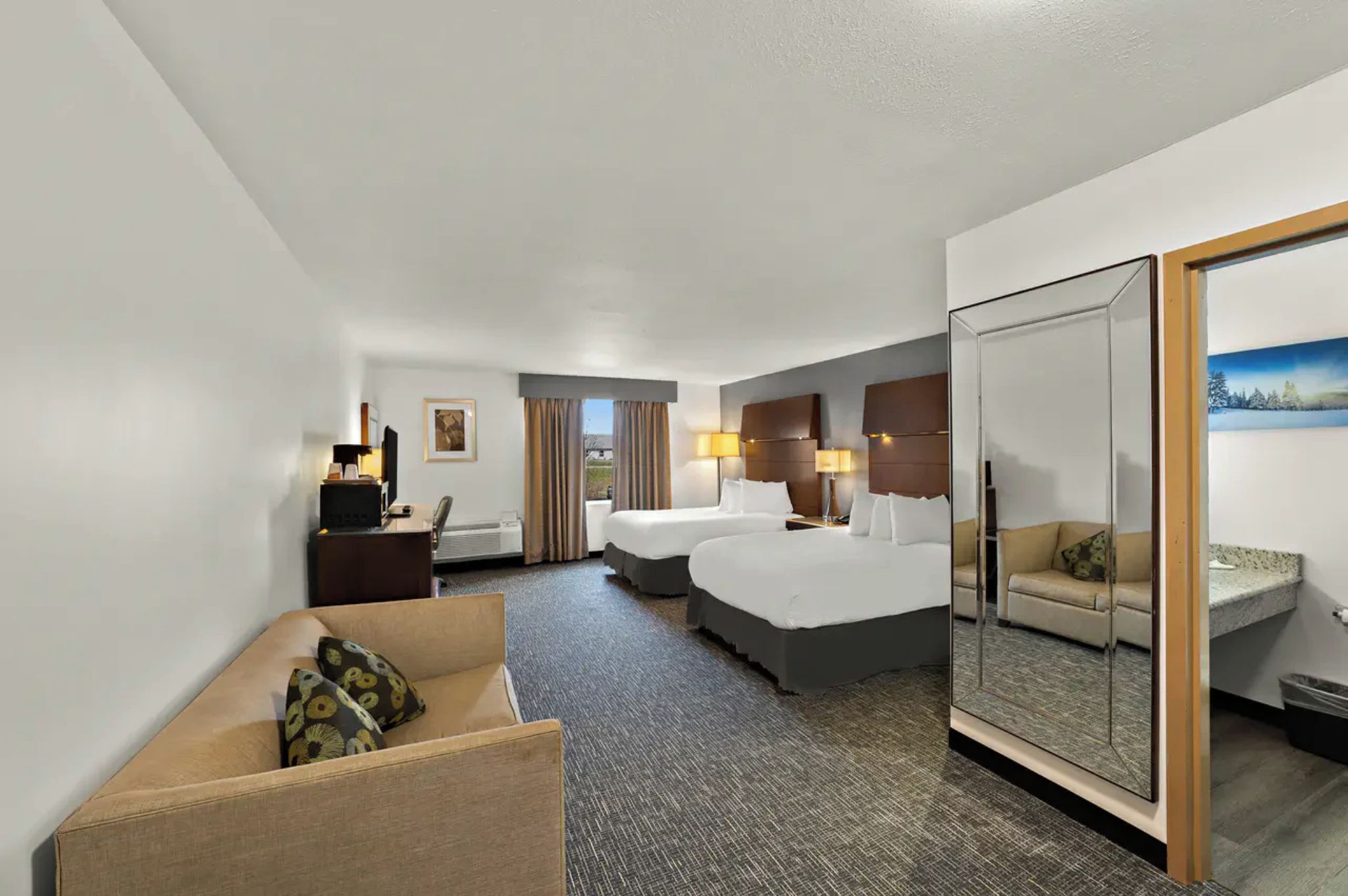 Een hotelkamer met twee bedden, een bureau, een bank, een spiegel en uitzicht op een besneeerd landschap.