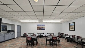 Ein Konferenzraum mit einem gemusterten Teppich, Tischen, Stühlen, einem Bild an der Wand und einer Küchenzeile.