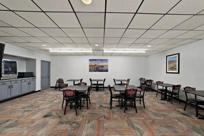 Un salón de conferencias con alfombra estampada, mesas, sillas, un cuadro en la pared y una zona de kitchenette.