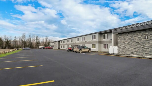 A parking lot with several cars, a building with a stone facade, and a clear sky. - Quality Inn & Suites Caribou (Caribou)