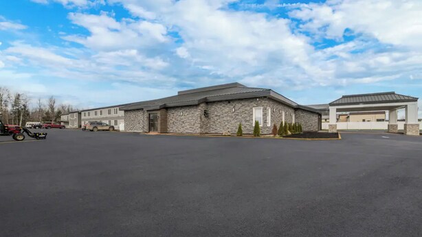 A building with a stone facade, a parking lot, and a clear sky. - Quality Inn & Suites Caribou (Caribou)