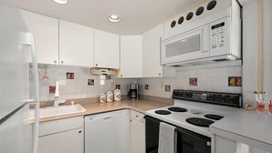 A modern kitchen with white cabinets, a microwave, a stove, and a coffee maker.