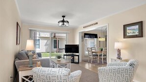 A living room with a sofa, two patterned armchairs, a coffee table, a TV, and a dining area with chairs and a table.