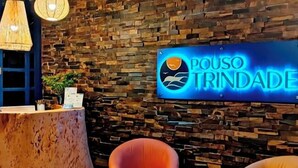 A reception area with a stone wall, a neon sign reading "POUSO TRINDADE", and two orange chairs. - Pouso Trindade (Paraty)