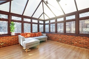 Relax in this serene sunroom with a high ceiling and large windows, featuring a brick wall and wooden flooring.