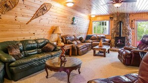A cozy cabin interior with a stone fireplace, leather sofas, and a wooden ceiling.