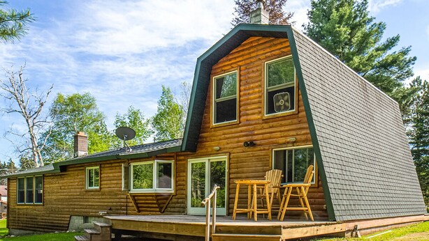 A log cabin with a steeply pitched roof, a chimney, and a deck with outdoor seating.